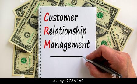 Male hand writing 'customer relationship management' on white note, on white background. Dollar bills. Stock Photo