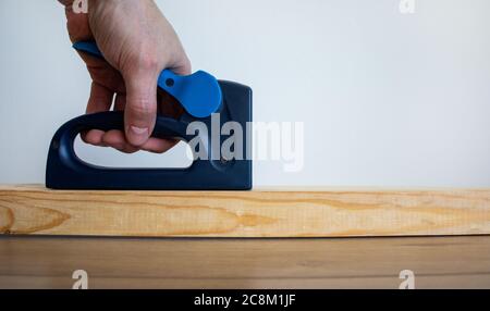 A male hand holds a construction stapler on a wooden bar. Beautiful white background. Copy space. Stock Photo