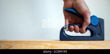 A male hand holds a construction stapler on a wooden bar. Beautiful white background. Copy space. Stock Photo
