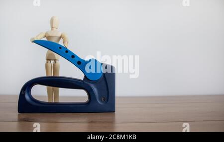 A construction stapler on a wooden table. Wooden model of human. Beautiful white background. Copy space. Stock Photo