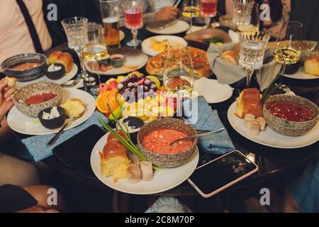 Focus on hands serving dishes of meat and vegetables to a group of friends gathered around a table on a summer terrace. Stock Photo