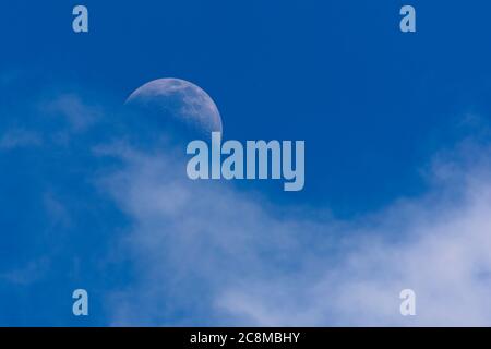 Half moon hidden in the clouds in the middle of the afternoon without the sun going down Stock Photo