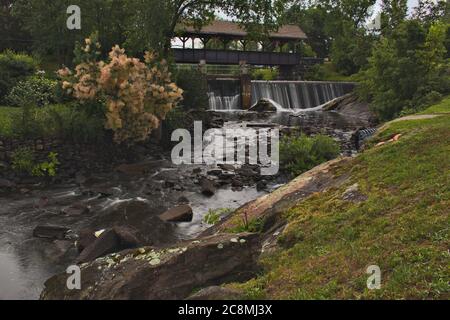 covered bridge with a small waterfall underneath, leading to a river Stock Photo