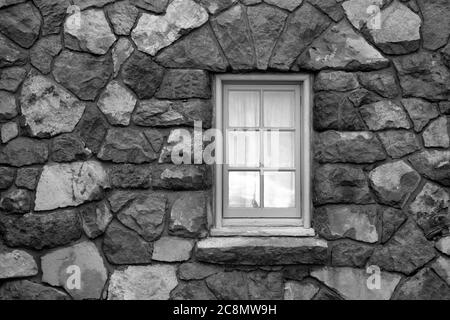 A small six-pane window in an enormous stone wall. Stock Photo