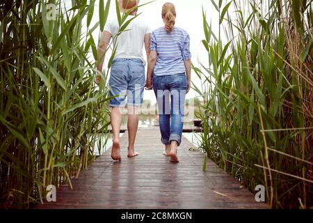 young couple walking barefoot toward lake, holding hands Stock Photo