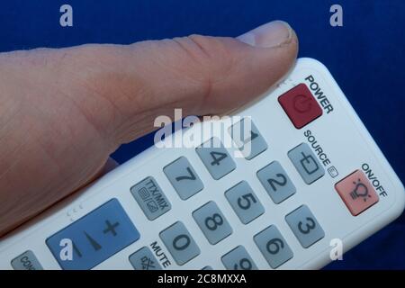 hand with a white remote control with multi-colored buttons Stock Photo
