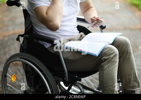 Man sit in wheelchair and take note in notebook in park. Stock Photo