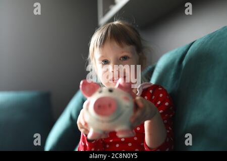 Child in red dress hold pink piggy bank in her hands. Stock Photo