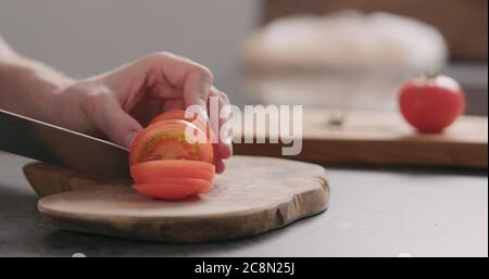 Man cutting tomatoe on concrete countertop side view Stock Photo