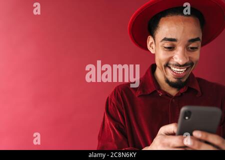 Handsome smiling stylish young african man using mobile phone while standing isolated over red background Stock Photo