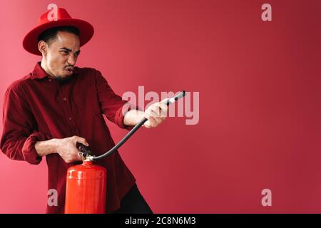 Image of a handsome african emotional young man posing isolated over red wall background holding fire extinguisher Stock Photo