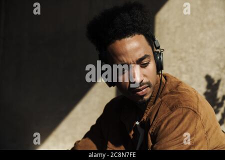 Photo closeup of serious african american man with mustache using headphones in bright room Stock Photo