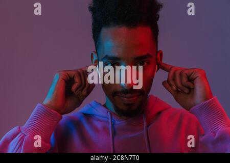 Portrait of bearded african american man in colorful hoodie listening to music with earpods isolated over violet background Stock Photo