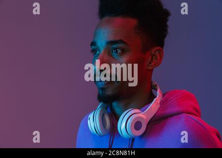 Portrait of casual african american man in colorful hoodie posing with headphones isolated over violet background Stock Photo