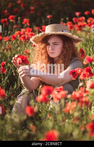 Young beautiful red-hear girl in red poppy field Stock Photo