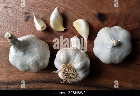 Garlic bulbs with loose cloves close up on a wooden chopping board under natural light. Stock Photo