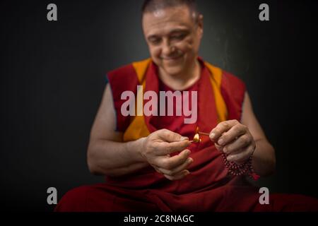 Buddhist monk in red kesa, holding an incense stick with incense in his hand Stock Photo