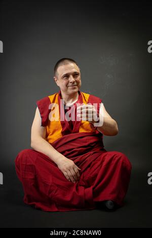 Buddhist monk in red kesa, holding an incense stick with incense in his hand Stock Photo