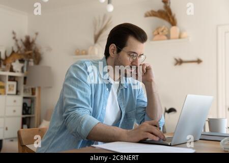 Concentrated Caucasian man sit at home desk working on laptop Stock Photo