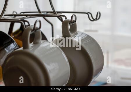Coffee Mugs Hanging on Rack. White porcelain cups on metal hooks. Shooting at eye level. Selective focus. Stock Photo