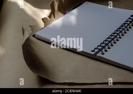Open spring-bound notebook in sunlight. New diary with blank pages on torn wrapping paper. Side view at an angle. Selective focus. Stock Photo
