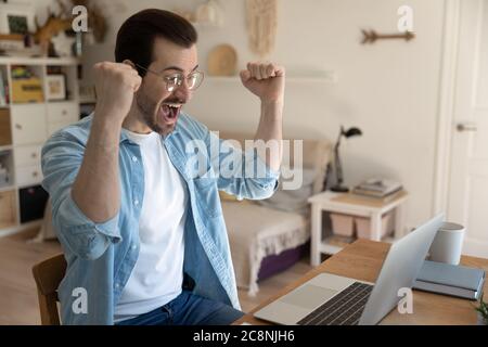 Excited young man triumph reading news on laptop Stock Photo