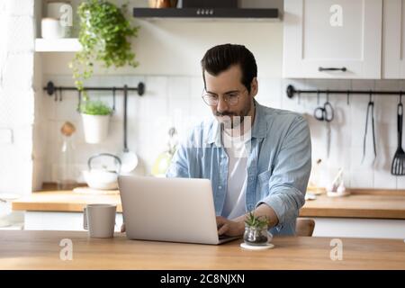 Caucasian man sit in kitchen working on laptop Stock Photo