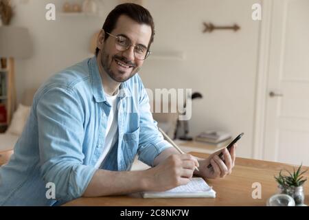 Portrait of smiling young man use cellphone making notes Stock Photo