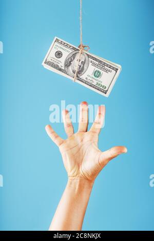 The hand reaches for the money suspended on a rope, on a blue background. Stock Photo