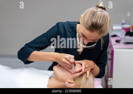 Cosmetology cabinet client lies on couch. Beautician applies marking on eyebrows. Preparation for the procedure of permanent eyebrow makeup. Free space. Beauty industry Stock Photo