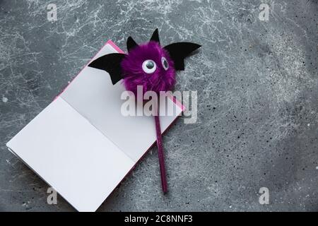 Trendy purple bat pencil and pink notebook for notes on grey background. Halloween still life. Flat lay Stock Photo