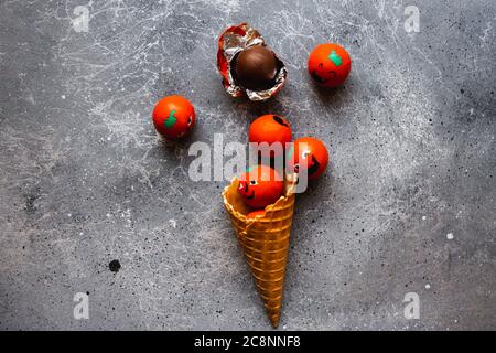 Waffle cone is filled with candies Halloween pumpkins on the grey background Stock Photo