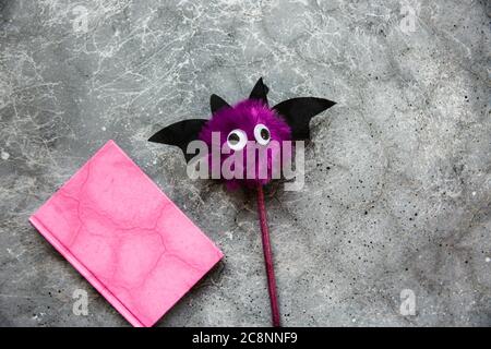 Trendy purple bat pencil and pink notebook for notes on grey background. Halloween still life. Flat lay Stock Photo
