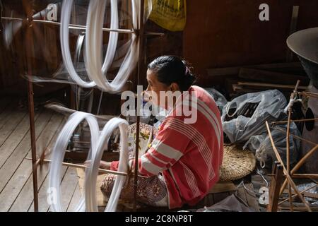 Inle Lake, Myanmar - February 2020: Burmese  woman spins thread on a traditional spinning wheel in local village. Lotus and silk fibres are woven for Stock Photo