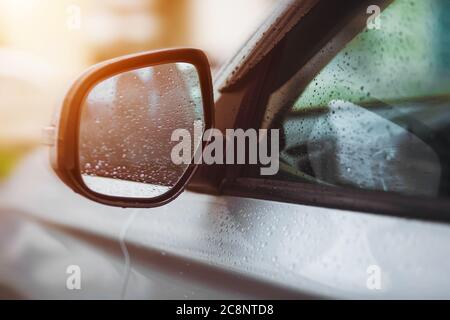 A silver car with raindrops on the windows and rearview mirror is driving fast, illuminated by the sun. Transport. Stock Photo