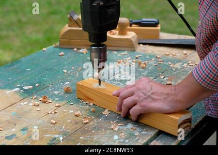 Carpenter using drill machine to make a hole on wooden plank, close up view. DIY, woodworking, joinery shop concept. Stock Photo