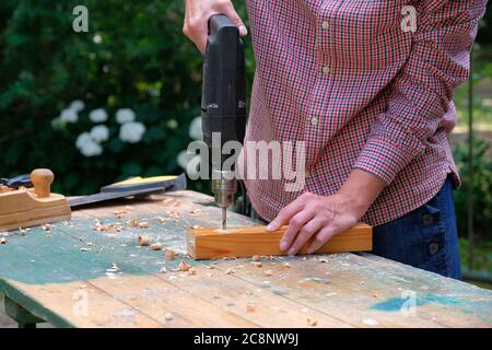 Carpenter drilling wooden plank using electric drill machine, closeup view. Craftswoman working outdoors. DIY, woodworking concept. Stock Photo