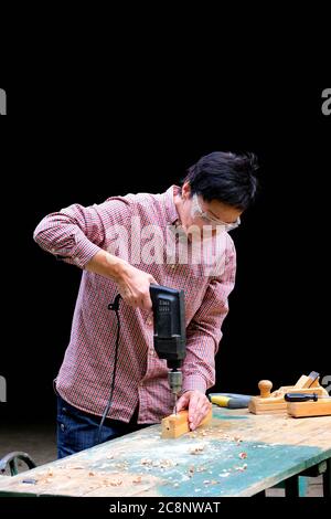 Craftswoman drilling a hole with an electric drill machine in wooden plank. Woodwork, DIY, gender equality concept. Stock Photo
