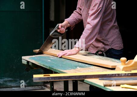 Craftswoman cutting plank with handsaw in workshop. Carpentry, construction, woodworking concept. Stock Photo