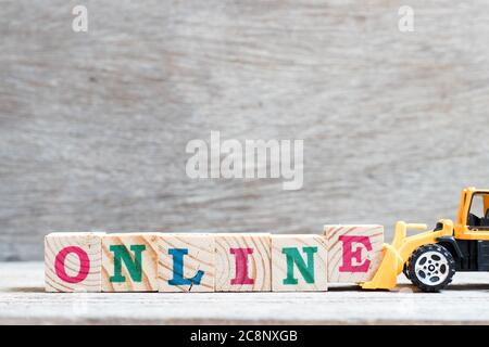 Toy bulldozer hold letter block e to complete word online on wood background Stock Photo