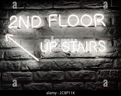 there's a neon sign on the wall that says '2nd Floor upstairs' Stock Photo