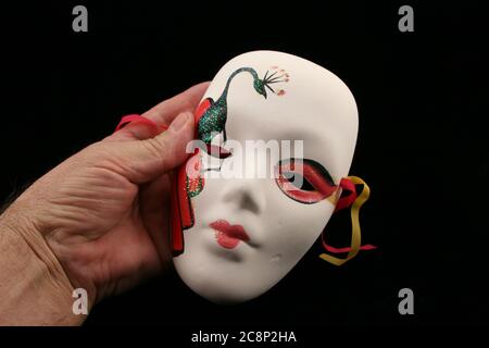 Man's hand holding Mardi Gras small face mask on a black background. Stock Photo