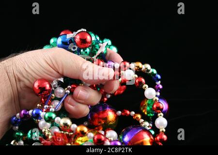 Woman's hand holding Mardi Gras beads on a black background. Stock Photo