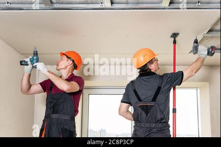 Installation of drywall. Workers are using screws and a screwdriver to attach plasterboard to the ceiling. Stock Photo