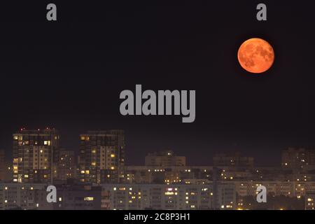 Bright yellow moon in dark night sky above the city. Background Stock Photo