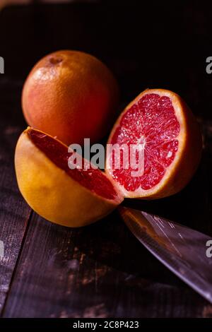 still life with juicy and fresh cut seasonal grapefruits on wooden table and kitchen knife Stock Photo
