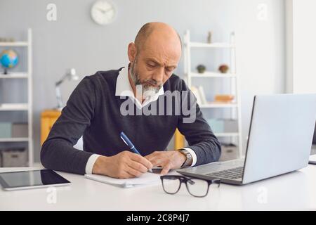 Working and studying from home. Thoughtful mature man taking notes during online business meeting or webinar Stock Photo