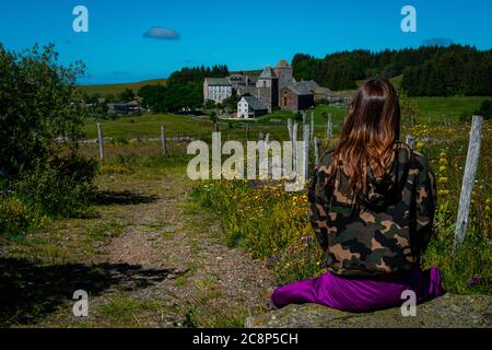 young woman looking towards Aubrac village ,a stage on the compostelle walk or saint James way, with wild flowers in foreground. Stock Photo