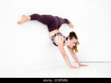 Young gymnast doing a handstand split exercise balancing against a white wall in a gym in a healthy active lifestyle and fitness concept Stock Photo