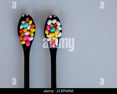 Multi colored sweet fennel sugar candy in black spoons against white background with copy space, isolated Stock Photo